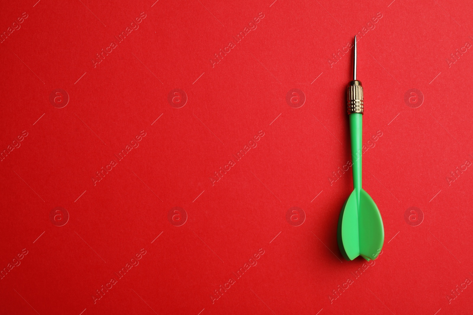 Photo of Green dart arrow on red background, top view with space for text