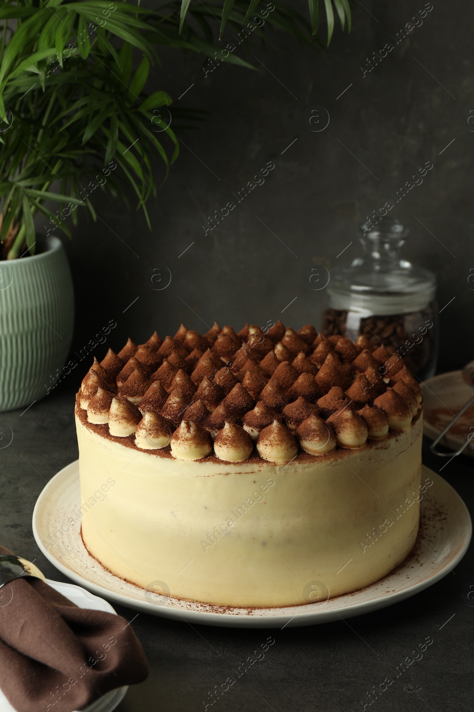 Photo of Delicious tiramisu cake with cocoa powder on black table