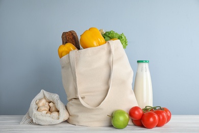 Shopping bag with fresh vegetables and other products on white wooden table against light blue background