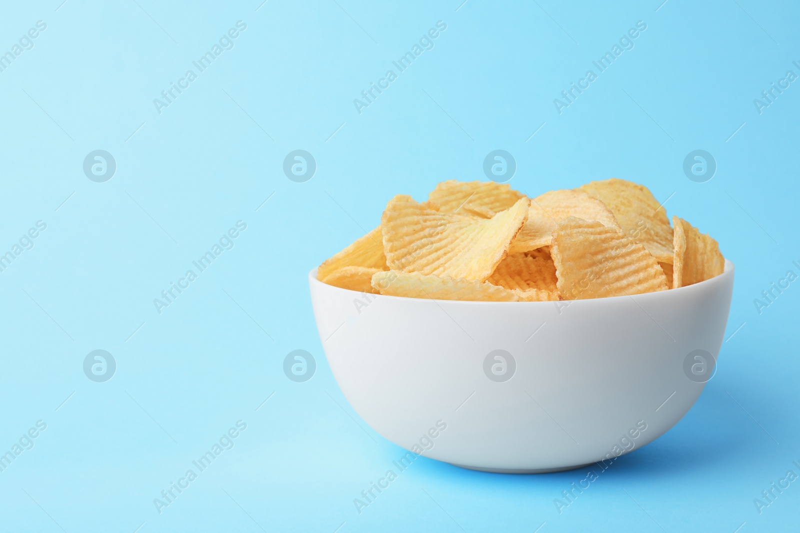 Photo of Delicious crispy potato chips in bowl on color background, space for text