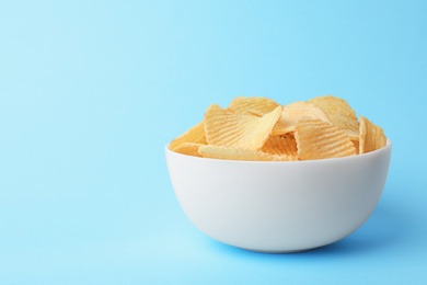Delicious crispy potato chips in bowl on color background, space for text