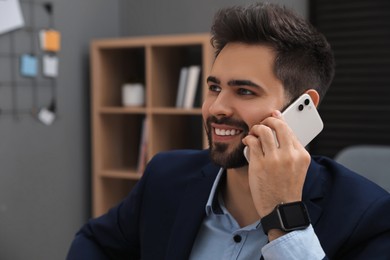 Photo of Happy young businessman wearing smart watch and talking on smartphone in office