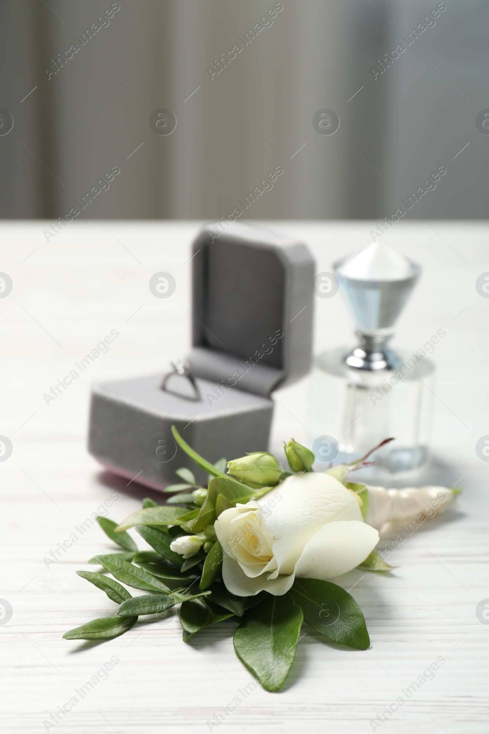 Photo of Wedding stuff. Stylish boutonniere, perfume and ring on white wooden table, closeup