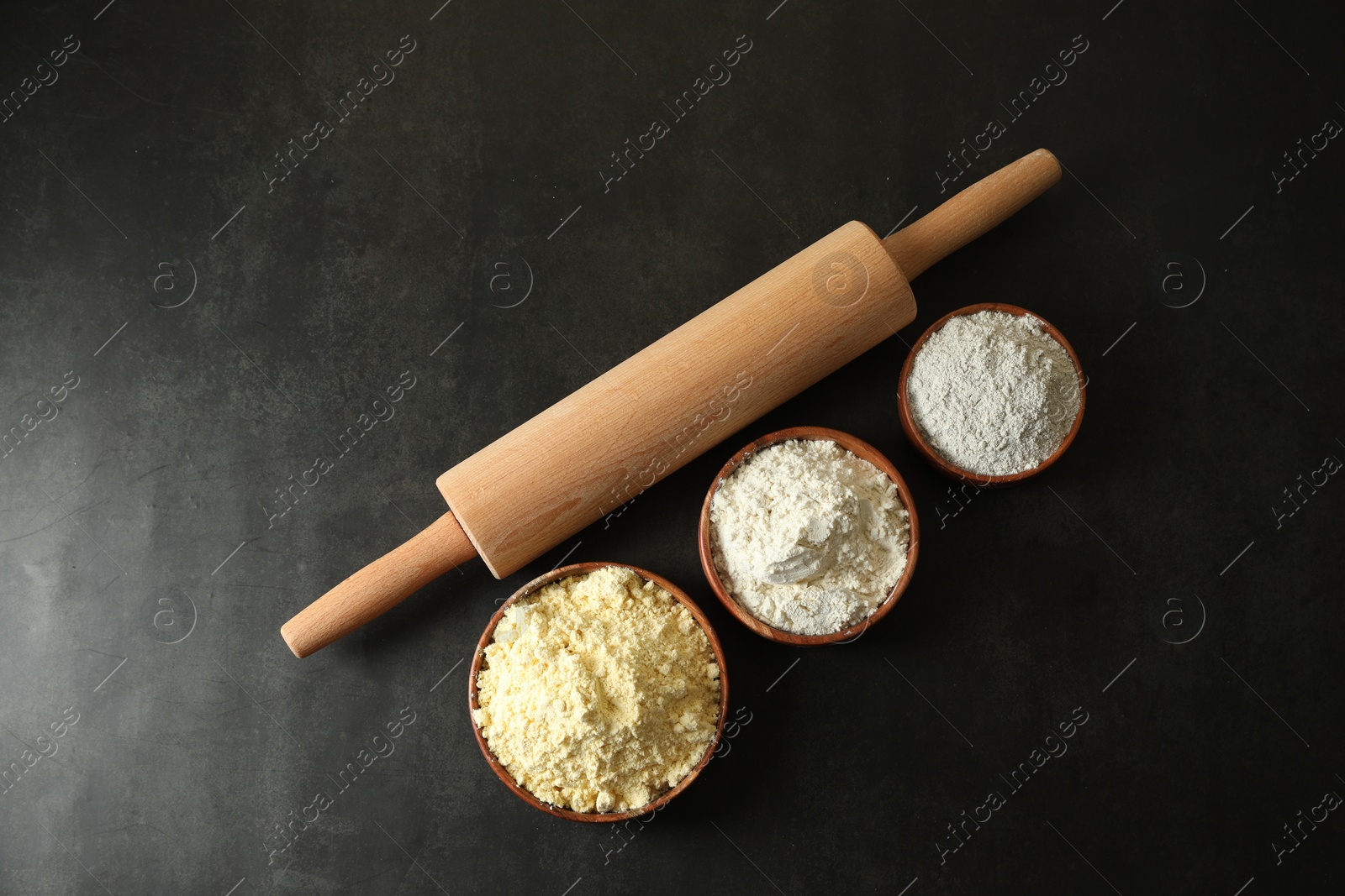 Photo of Rolling pin and different types of flour on black table, flat lay