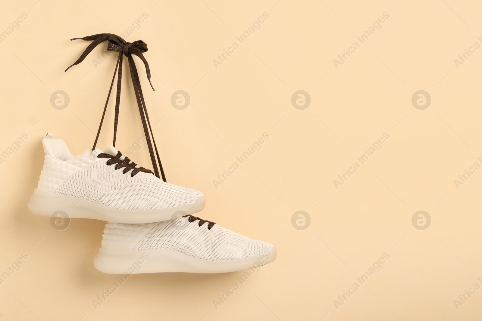 Photo of Stylish sneakers with brown shoe laces hanging on beige wall. Space for text
