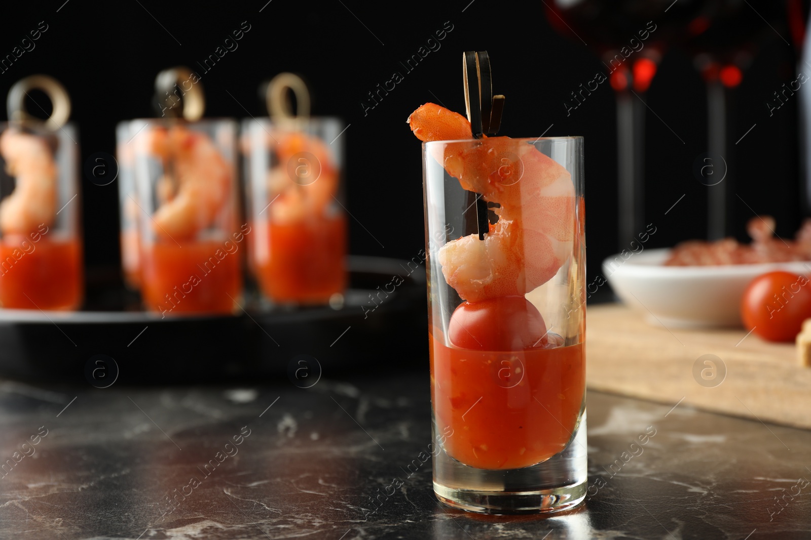 Photo of Tasty canape with shrimp, tomato and sauce in shot glass on black marble table, closeup. Space for text