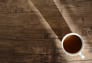 Photo of Cup of coffee on wooden table in morning, top view. Space for text