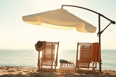 Wooden deck chairs, outdoor umbrella and beach accessories near sea. Summer vacation