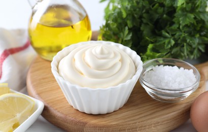 Photo of Fresh mayonnaise sauce in bowl and ingredients on table, closeup