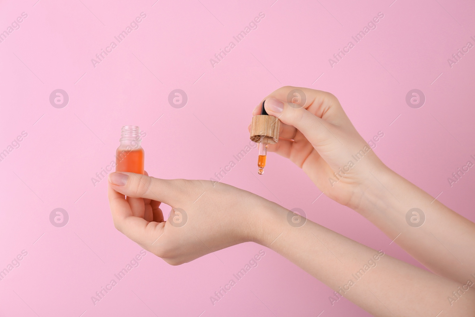 Photo of Woman applying essential oil onto wrist against pink background, closeup