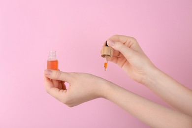 Woman applying essential oil onto wrist against pink background, closeup