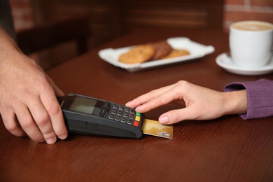 Woman using terminal for credit card payment in cafe, closeup