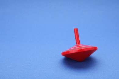 Photo of One bright spinning top on blue background, space for text. Toy whirligig