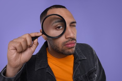 Photo of Man looking through magnifier glass on violet background