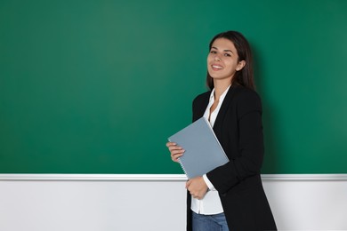Photo of Happy young teacher with books at blackboard in classroom. Space for text
