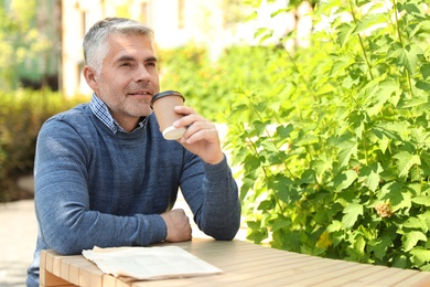 Photo of Handsome mature man sitting at table in park. Space for text