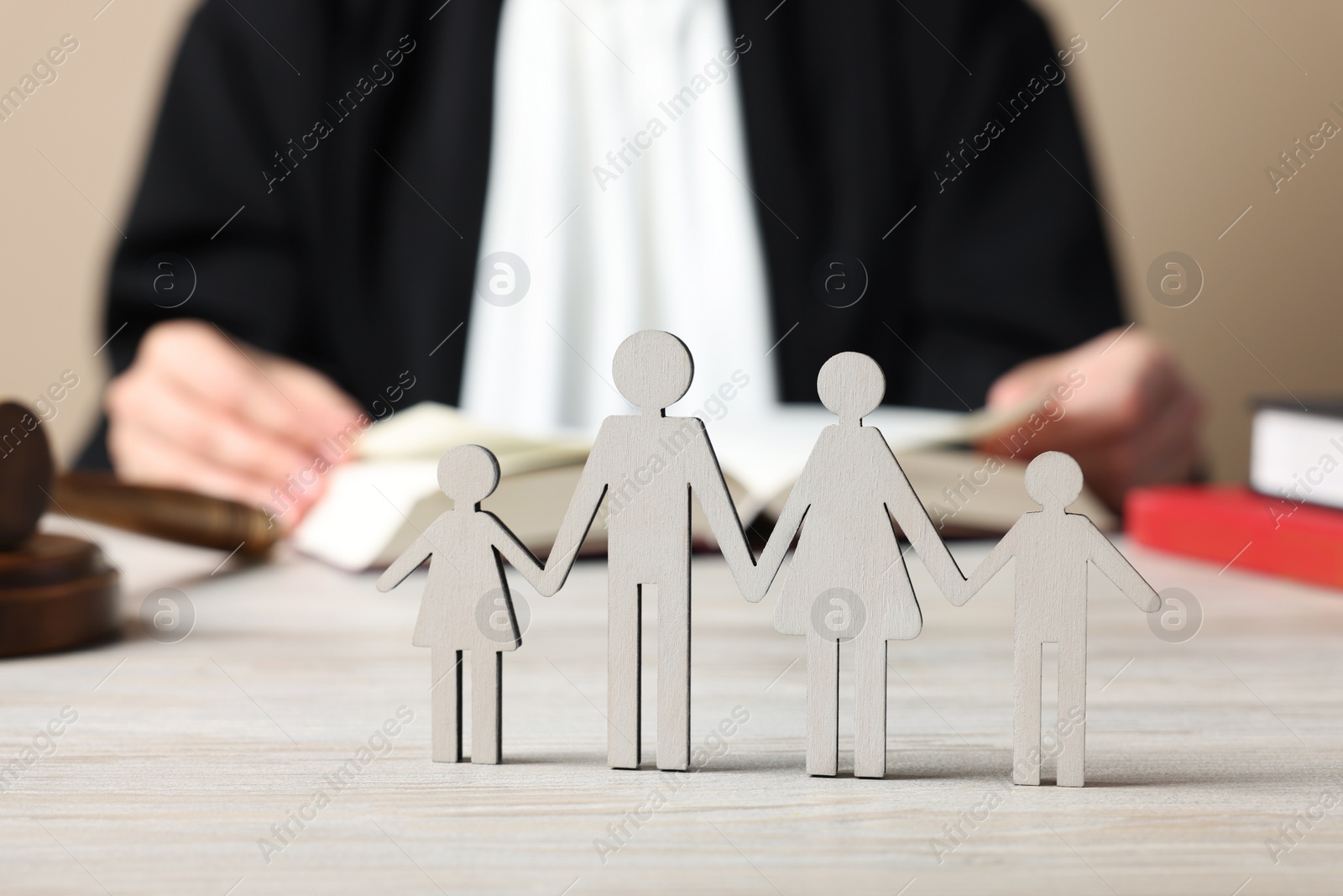 Photo of Family law. Judge with book sitting at white wooden table, focus on figure of parents and children