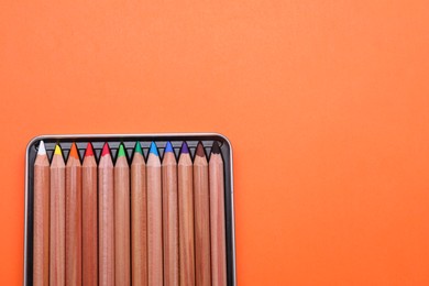 Photo of Box with many colorful pastel pencils on orange background, top view and space for text. Drawing supplies