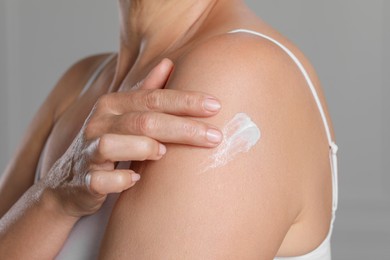 Woman applying body cream onto shoulder indoors, closeup