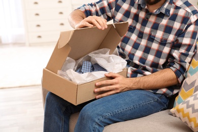 Photo of Young man opening parcel at home, closeup