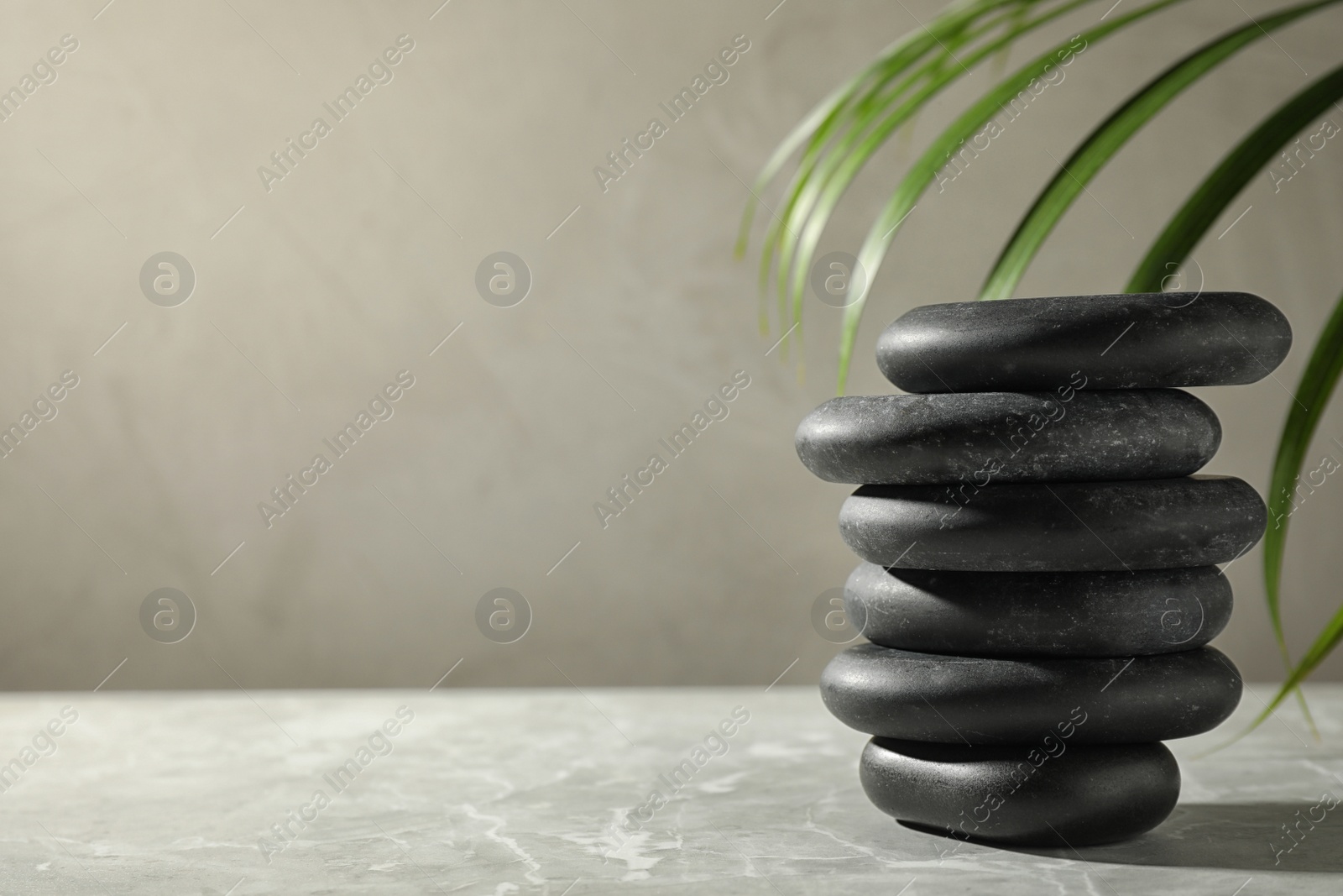 Photo of Stack of spa stones and palm leaf on grey table, space for text