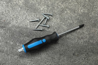 Photo of Screwdriver with black handle and screws on grey table, flat lay