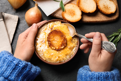 Photo of Woman eating tasty homemade french onion soup at black table, top view
