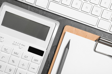 Photo of Calculator, clipboard and keyboard on dark grey table, flat lay. Tax accounting