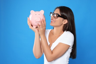 Photo of Young woman in eyeglasses with piggy bank on light blue background