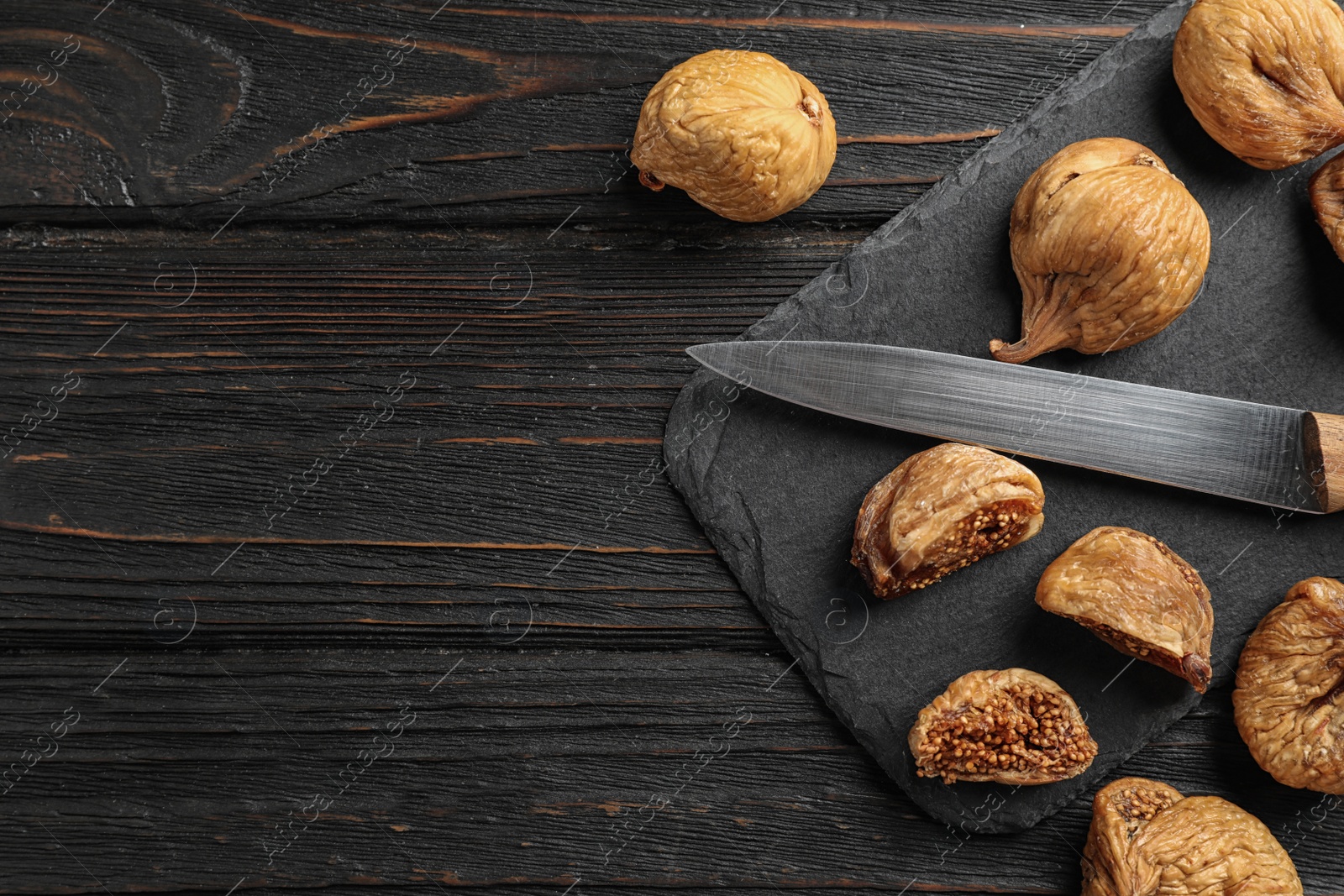 Photo of Slate plate with tasty dried figs and knife on black wooden table, flat lay. Space for text