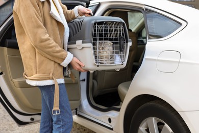 Photo of Woman holding carrier with cute Scottish fold cat near car outdoors, closeup