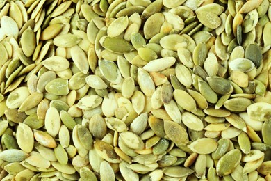 Photo of Many peeled pumpkin seeds as background, top view