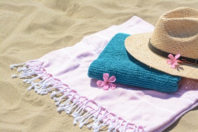 Photo of Blanket with towel, stylish straw hat and flowers on sand outdoors. Beach accessories