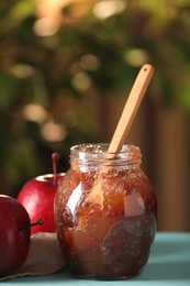 Photo of Glass jar with delicious apple jam and fresh fruits on light blue wooden table against blurred background, closeup. Space for text