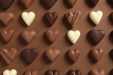 Photo of Beautiful heart shaped chocolate candies on brown background, flat lay