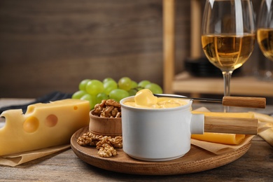 Pot of tasty cheese fondue and products on wooden table