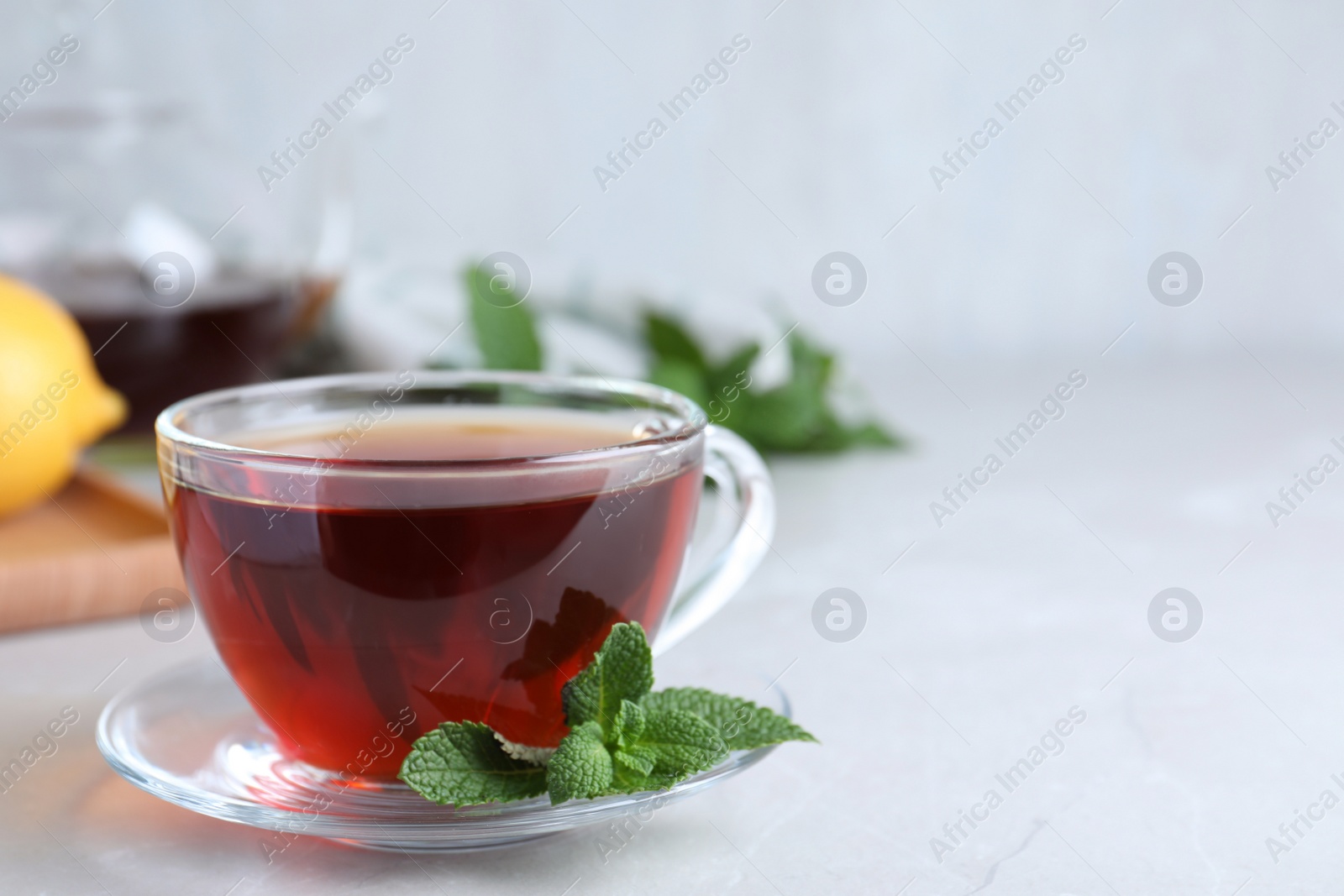 Photo of Cup of hot aromatic tea with mint on light grey marble table. Space for text