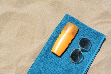 Photo of Soft blue beach towel with bottle of sunblock and sunglasses on sand, flat lay. Space for text