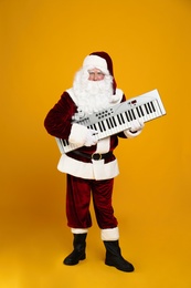 Photo of Santa Claus with synthesizer on yellow background. Christmas music