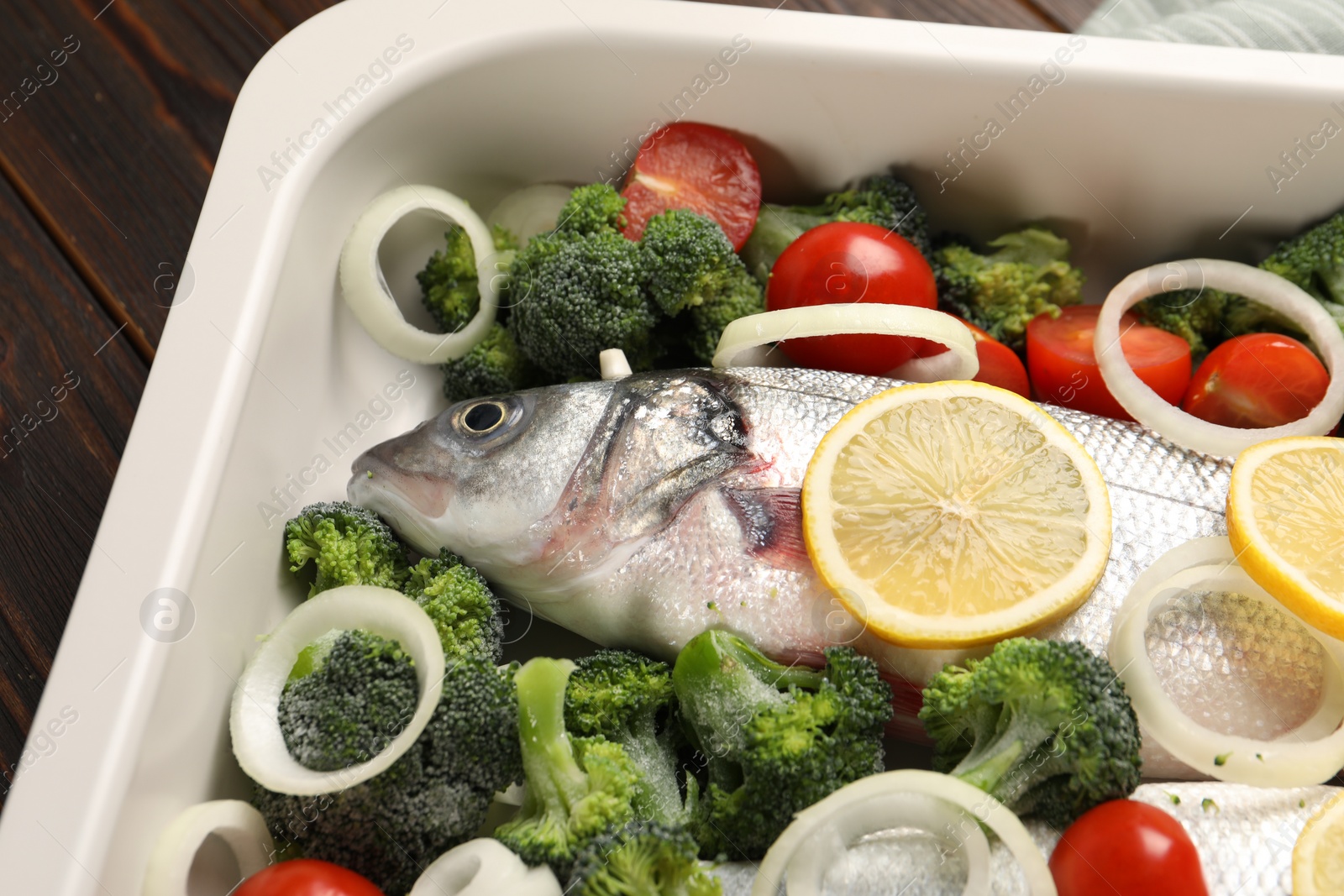 Photo of Raw fish with vegetables and lemon in baking dish on table