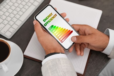 Energy efficiency. Man using smartphone with colorful rating on display at table, closeup