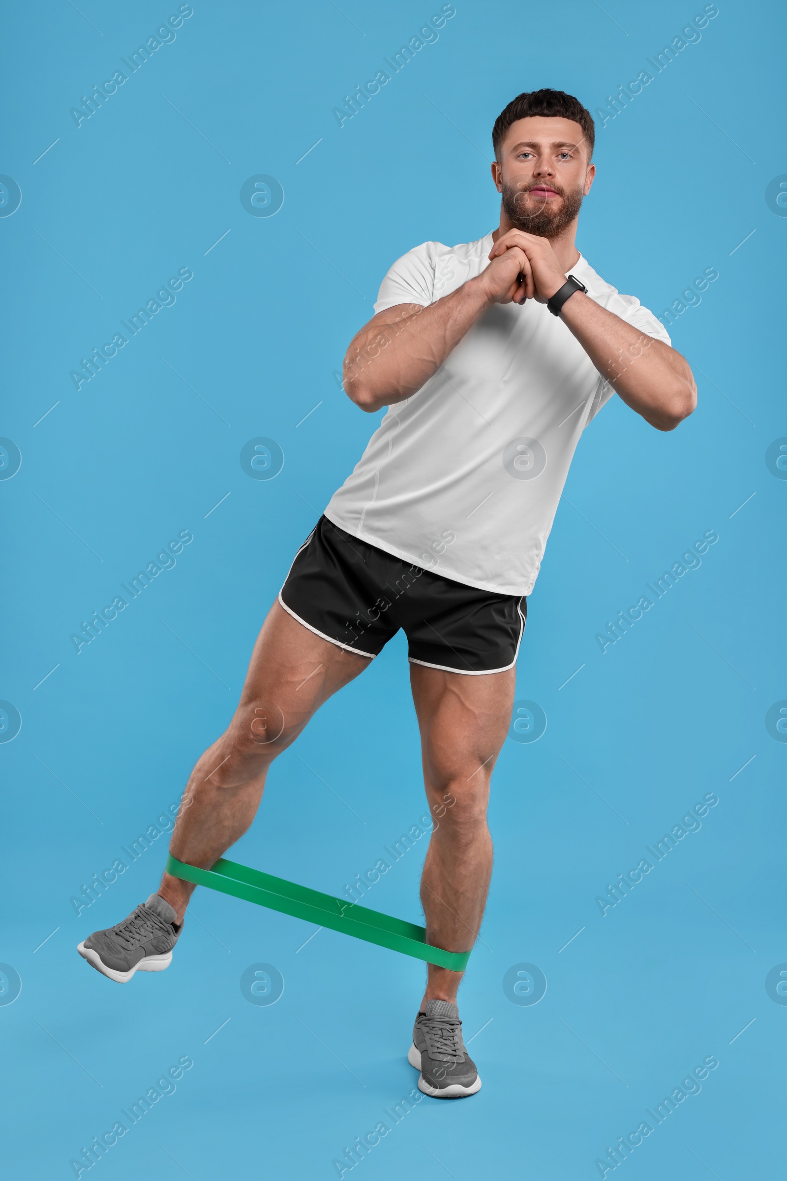 Photo of Young man exercising with elastic resistance band on light blue background