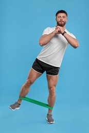 Photo of Young man exercising with elastic resistance band on light blue background