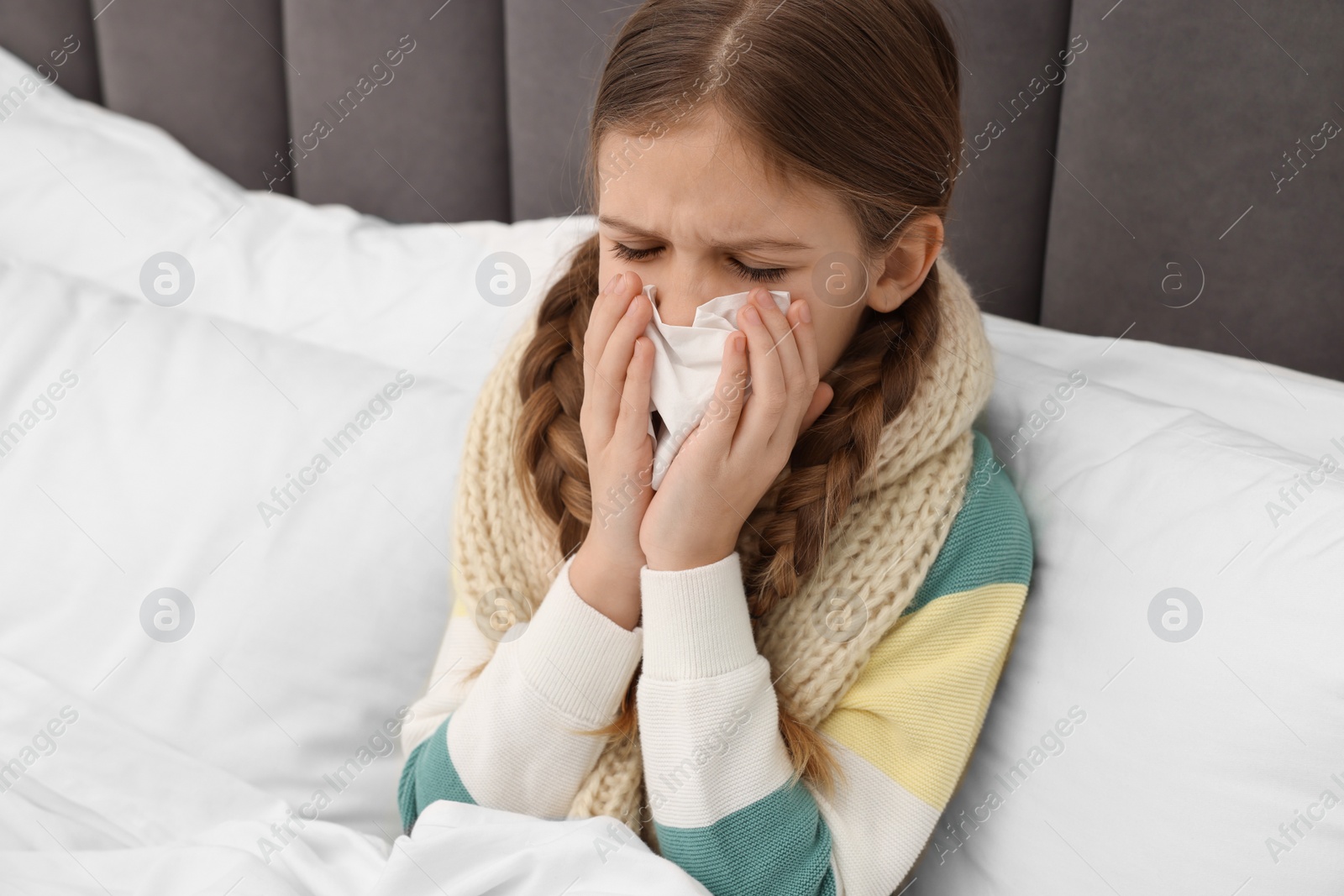 Photo of Sick girl with tissue coughing on bed at home