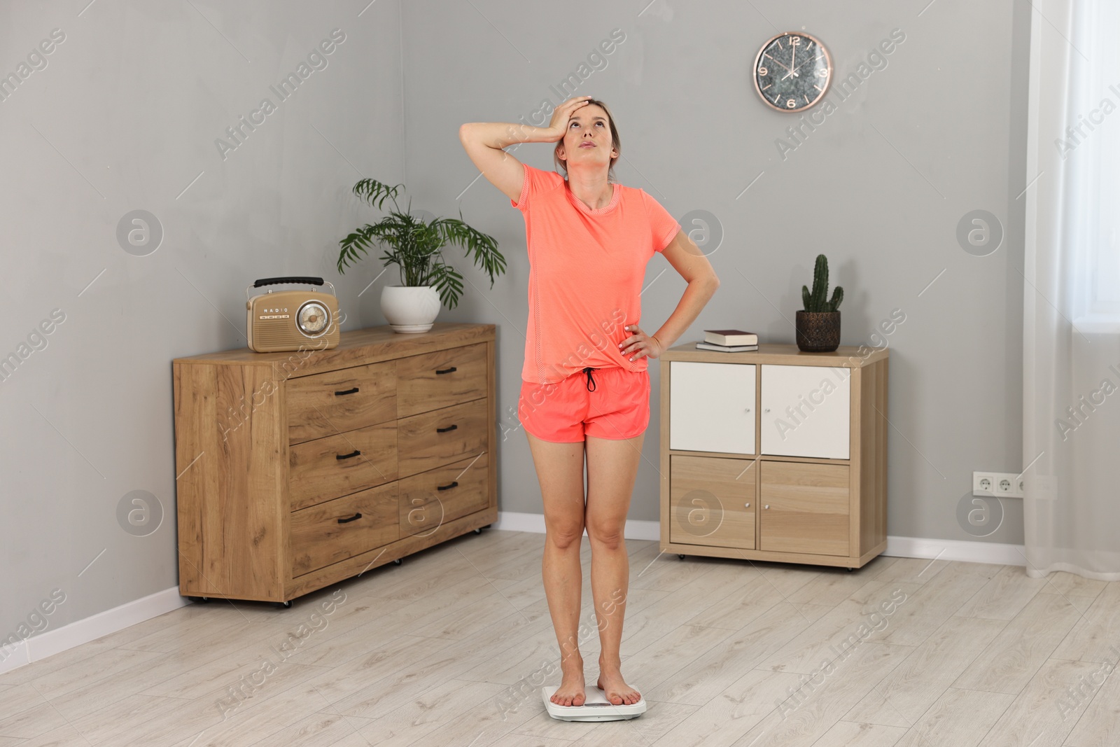 Photo of Unhappy woman in sportswear standing on floor scales at home