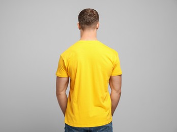 Man wearing yellow t-shirt on light grey background, back view. Mockup for design