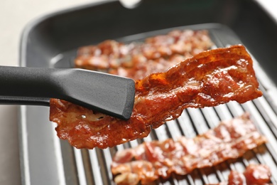 Tongs with fried bacon over table, closeup