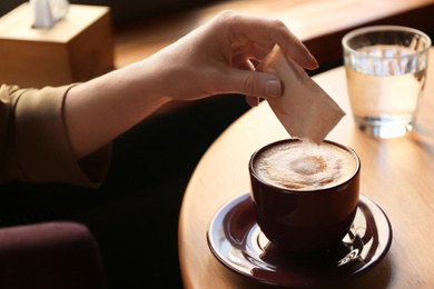 Photo of Woman adding sugar to aromatic coffee at table in cafe, closeup