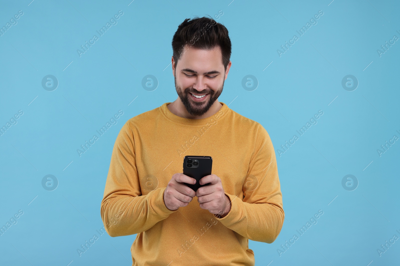 Photo of Happy young man using smartphone on light blue background