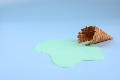 Photo of Melted ice cream and wafer cone on light blue background. Space for text